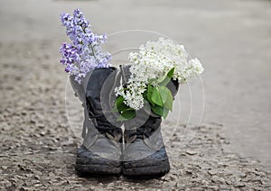 Bouquet of white and lilac flowers in dirty soldier`s boots in the spring garden