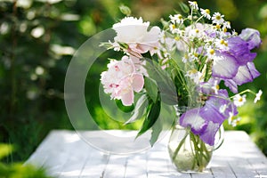 Bouquet of white peonies, chamomiles and iris flowers in glass vase. Summer background