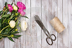 Bouquet of white and pink peonies flowers, twine and vintage scissors on white painted wooden planks.Top view.