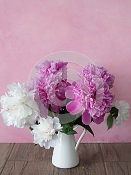 Bouquet of white and pink peonies in a white jug on a pink background. Close-up, selective focus