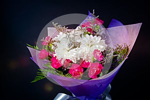 Bouquet of white and red flowers in purple paper on black background