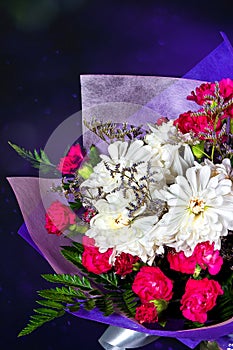 Bouquet of white and red flowers in purple paper on black background, vertical photo