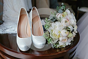 Bouquet of white roses and elegant wedding shoes on wooden table