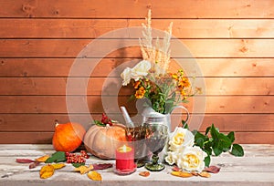 Bouquet of white roses, helenium and dry grass in watering can, candles, pumpkins, glasses of red wine and white roses near on
