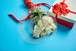 Bouquet of white roses with red bow on blue background. Boxed gift on side