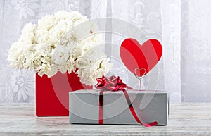 A bouquet of white roses in a red box and a figure of a heart from red paper for inscription on a white background.