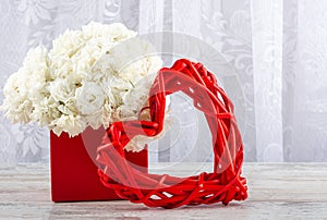 A bouquet of white roses in a red box and a photo frame a heart made of red rattan, close-up.