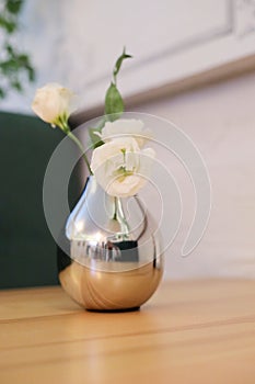 Bouquet of white small delicate flowers in silver vase on wooden table agains pink stone wall. Copy space Minimal style. Template