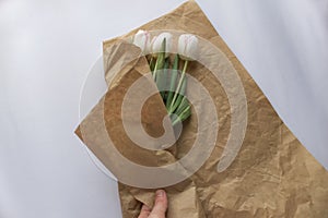 Bouquet of white tulip flowers is wrapped by the girl`s hand in craft paper