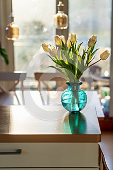 A bouquet of white tulips in a blue green glass vase in bright morning sun. Modern interior design, fresh spring flowers