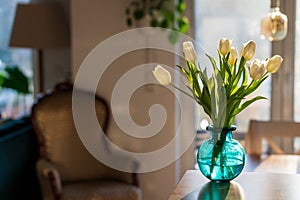 A bouquet of white tulips in a blue green glass vase in bright morning sun. Modern interior design, fresh spring flowers concept