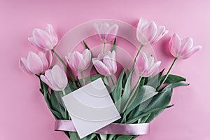 Bouquet of white tulips flowers and sheet of paper over light pink background. Greeting card or wedding invitation.