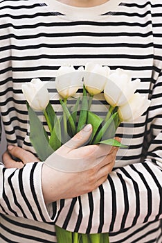 A bouquet of white tulips in hands on a background in the form of  horizontal white stripes.