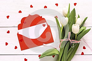 Bouquet of white tulips and a red envelope on white wooden background.