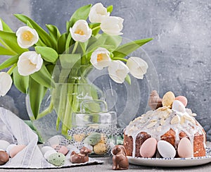 Bouquet of white tulips in a vase on a gray background. Shokloy eggs of different colors and Easter cake with cream, as a symbol