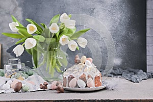 Bouquet of white tulips in a vase on a gray background. Shokloy eggs of different colors and Easter cake with cream, as a symbol