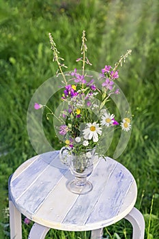 Bouquet of wild flowers in a glass vase on a rough wooden white bench, summer concept, farm rustic concept