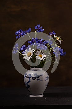Bouquet of wild flowers in a porcelain vase on a dark background