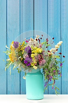 Bouquet of wild flowers in starm tin can vase on background blue wooden boards. Template for postcard Copy space lettering text or