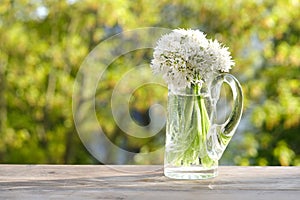bouquet of wild garlic flowers on old wooden table in garden, beautiful blurred natural landscape in background with green foliage