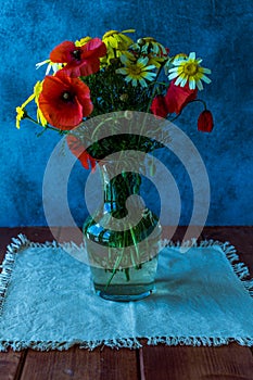 Bouquet of wild natural flowers in transparent glass vase on wooden table