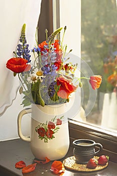 Bouquet of wild summer flowers on the window. Poppies, cornflowers, daisies and lupines in a rustic pot.