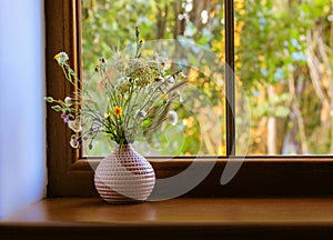 Bouquet of wildflowers in a pink vase on a wooden window sill at summer day