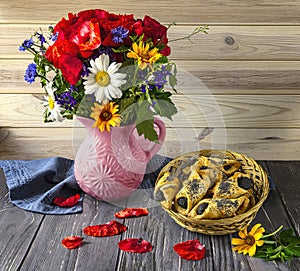 A bouquet of wildflowers with red poppies, a blue cup of coffee and poppy seed cookies in a straw basket.