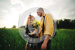 Bouquet of wildflowers in woman`s hand. Loving hipster couple walking in the field, kissing and holding hands, hugging, lying in