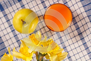Bouquet of yellow daffodils and apple, glass of orange juice on