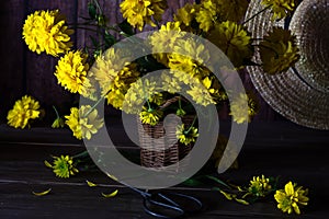 Bouquet of yellow dahlia flowers in wicker container on dark wooden background, still life with yellow dahlia flowers