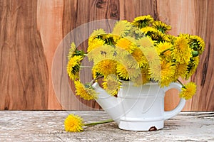 A bouquet of yellow dandelions in a white metal teapot, vase. Beautiful spring, summer background with a copy of the space