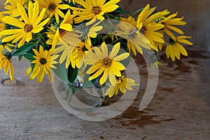 A bouquet of yellow Jerusalem artichoke flowers in a glass vase on a wooden background. Postcard with place for text. A simple