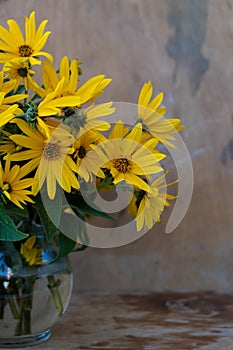 A bouquet of yellow Jerusalem artichoke flowers in a glass vase on a wooden background. Postcard with place for text. A