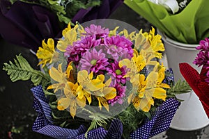 Bouquet yellow lilies and purple chrysanthemums, wrapped in a decorative package with a print