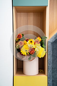 a bouquet of yellow and orange flowers in a hat box on a shelf in the closet.