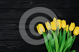 Bouquet of yellow spring tulip flowers on a black wooden background. Flat lay. Copy space. Mothers Day