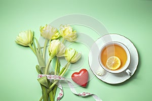 Bouquet of yellow tulips and a cup of tea with lemon close-up. Composition for Valentine`s Day, birthday.