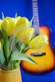 Bouquet of yellow tulips and guitar on blue background