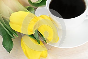 A bouquet of yellow tulips near a white saucer with a cup of coffee. Postcard. Wallpaper