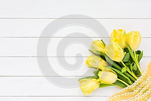 Bouquet of yellow tulips with ribbon on white wooden background. Top view