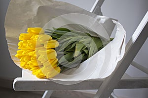 Bouquet of yellow tulips wrapped in white craft paper lies on a chair