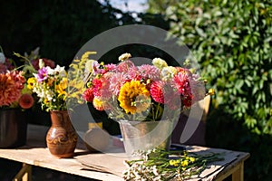 Bouquets of autumn flowers are on a wooden table outside in a bucket