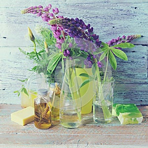 Bouquets of fresh flowers of purple lupine and chamomile in glass bottles with water, natural soap and aromatic oils
