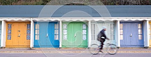 Bournemouth UK. Person cycling in front of colourful beach huts located on the promenade on the Bournemouth sea front.