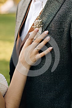 Boutonniere in boho style in the buttonhole of a jacket. Bride touches boutonniere