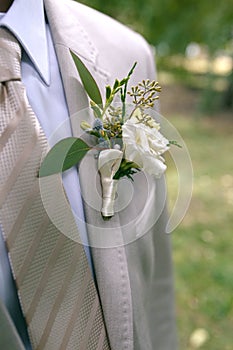 Boutonniere of white and yellow flowers with greens on lapel of a gray jacket