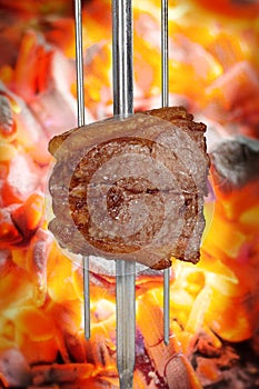 Bovine rump meat steak, traditional brazilian barbecue whole piece on skewer, on blurred ember background.