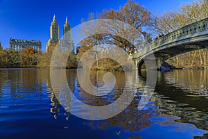 Bow Bridge in Central Park, New York in fall with Manhattan buildings in background and fallen leaves in the foreground