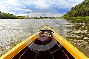 Bow of bright yellow canoe paddling on river surrounded by fores photo